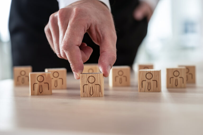 Human resources concept - businessman arranging wooden cubes with people icon on office desk.